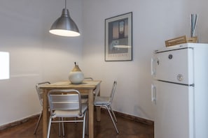 Uma cozinha compacta com uma mesa de jantar, cadeiras, luminária pendente, geladeira e um quadro na parede.