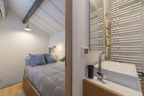 Quarto com cama, mesa de cabeceira, espelho, radiador e janela.