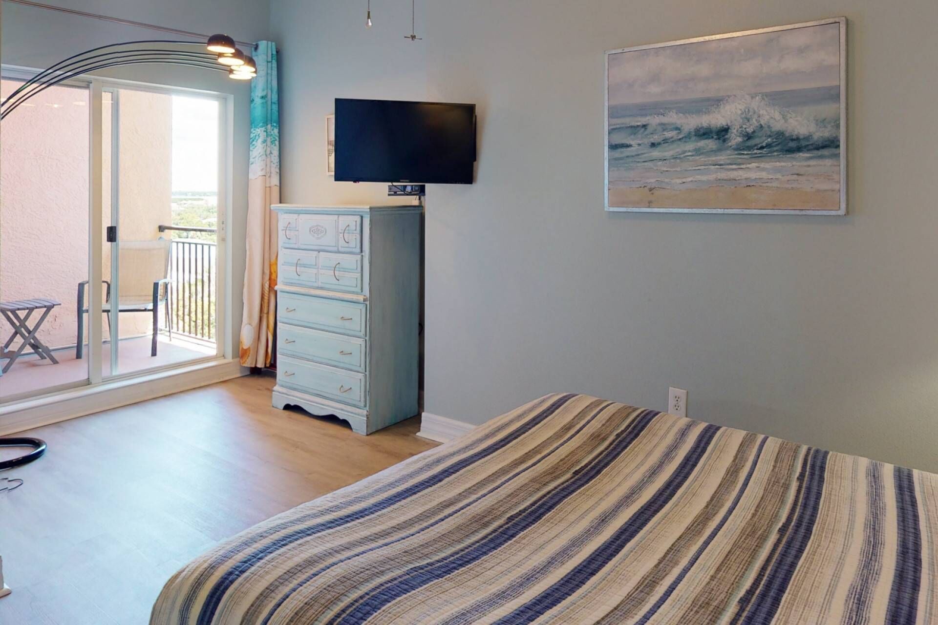 Un dormitorio con cama, cómoda, televisor y un cuadro de olas.