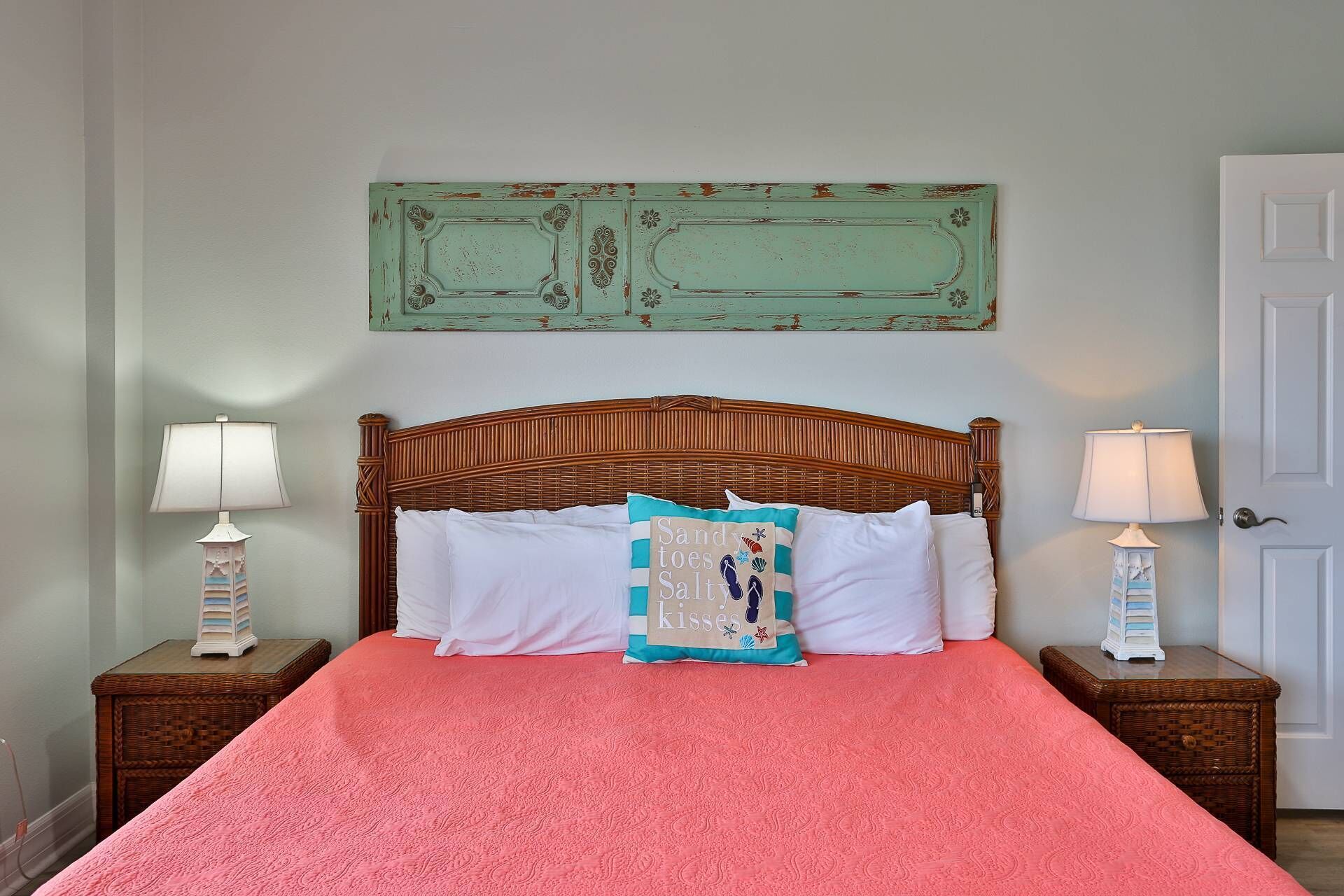 Un dormitorio con cabecera de madera, colcha rosa, dos mesitas de noche con lámparas y un adorno decorativo sobre la cama.