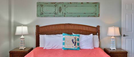 Un dormitorio con cabecera de madera, colcha rosa, dos mesitas de noche con lámparas y un adorno decorativo sobre la cama.