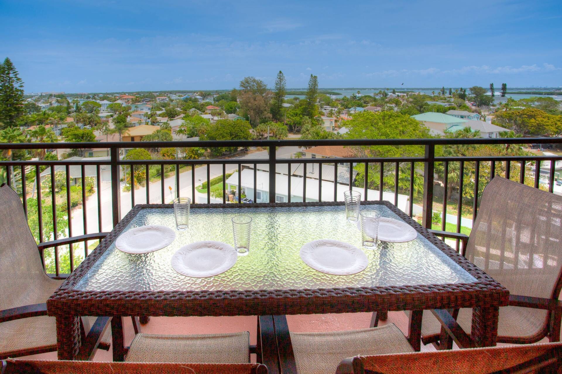A balcony with a glass table set for four, overlooking a residential area with houses and trees.