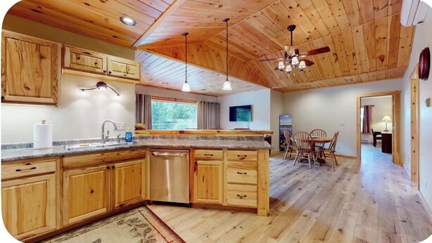 A kitchen with wooden cabinets, a dishwasher, and a dining area with a table and chairs. - Quiet, Bright, Open, Rustic Next to Park and Pond with Mountain Views!  Apt 201 (Lake Placid)