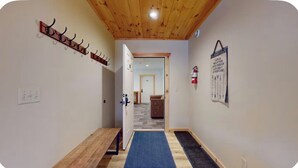 A hallway with a wooden ceiling, a coat rack, a blue mat, a fire extinguisher, and a door leading to another room. - Quiet, Bright, Open, Rustic Next to Park and Pond with Mountain Views!  Apt 201 (Lake Placid)