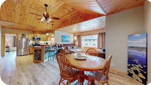 A spacious kitchen with wooden cabinets, a refrigerator, and a dining area with a wooden table and chairs. - Quiet, Bright, Open, Rustic Next to Park and Pond with Mountain Views!  Apt 201 (Lake Placid)