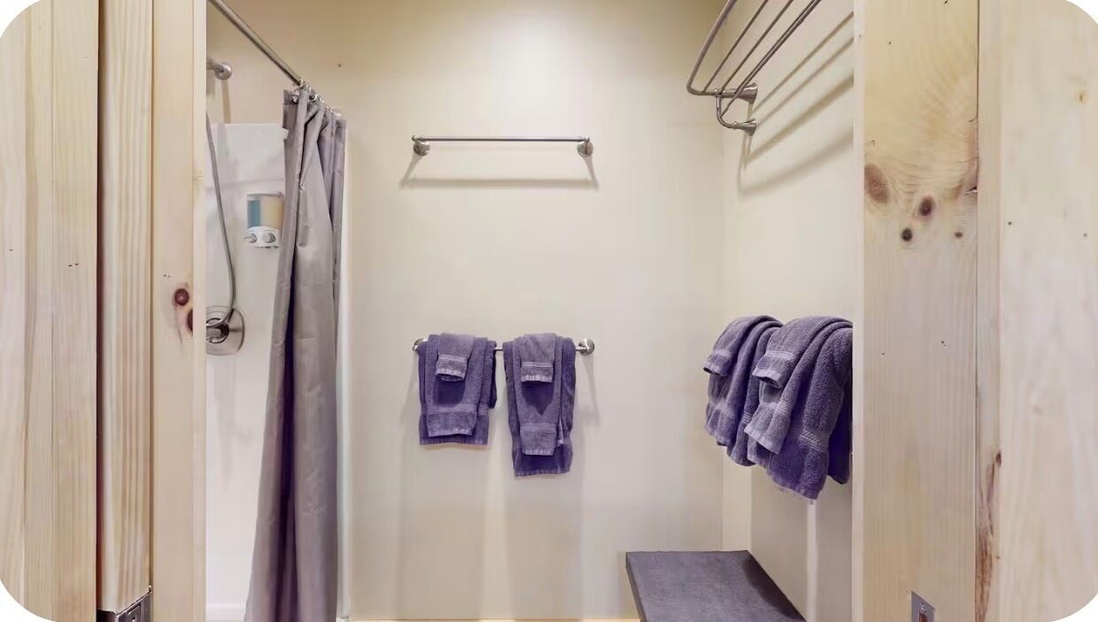 Un baño pequeño y cerrado con ducha, dos toallas colgadas de ganchos y un perchero en la pared.