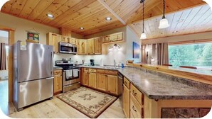 A kitchen with wooden cabinets, stainless steel appliances, granite countertops, and a large window. - Quiet, Bright, Open, Rustic Next to Park and Pond with Mountain Views!  Apt 201 (Lake Placid)