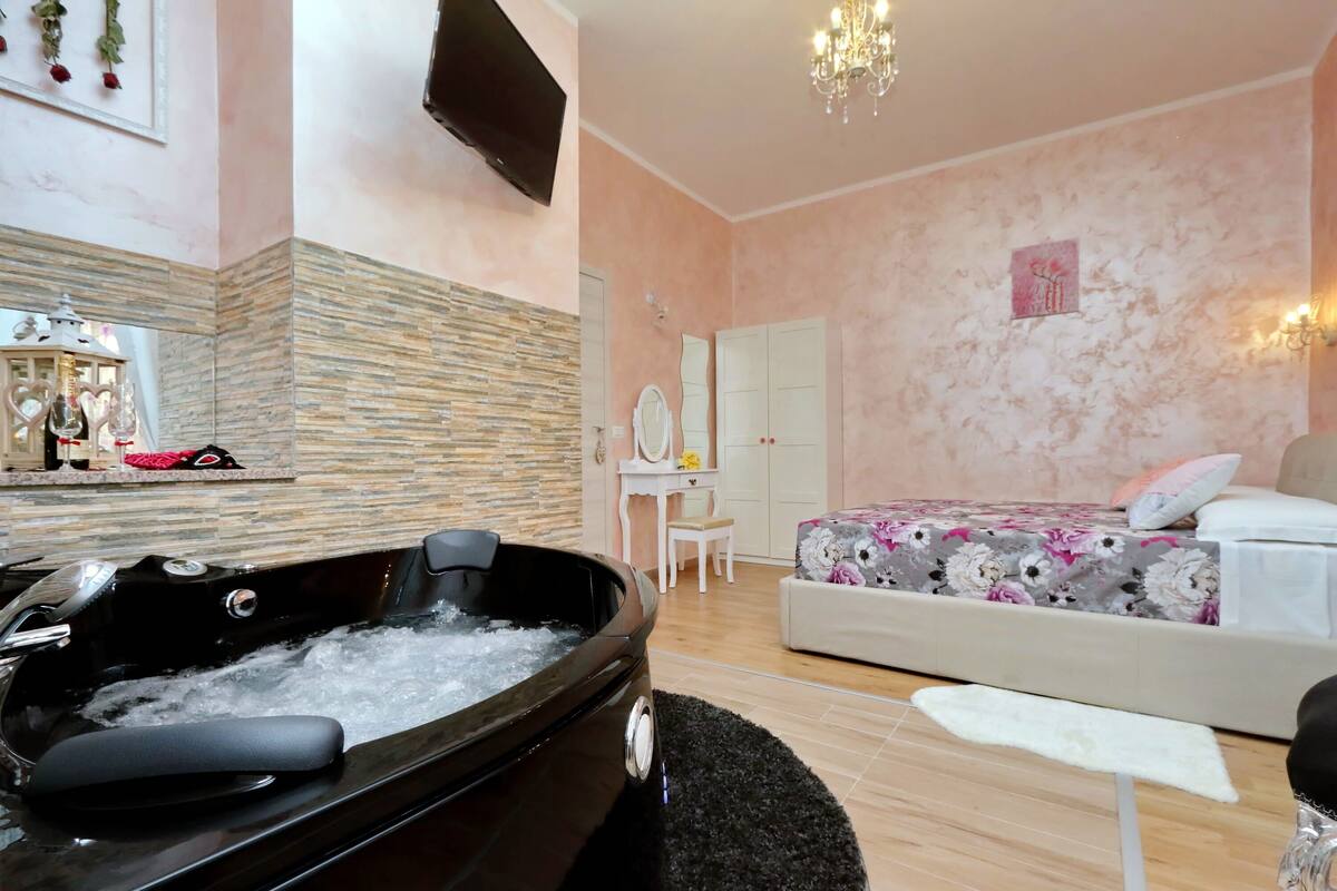 A bedroom with a large bed, a vanity with a mirror, and a bathtub filled with water.