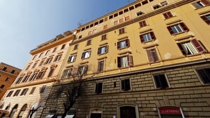 Un edificio de varios pisos con fachada amarilla, múltiples ventanas y un letrero visible de 'Generali'.