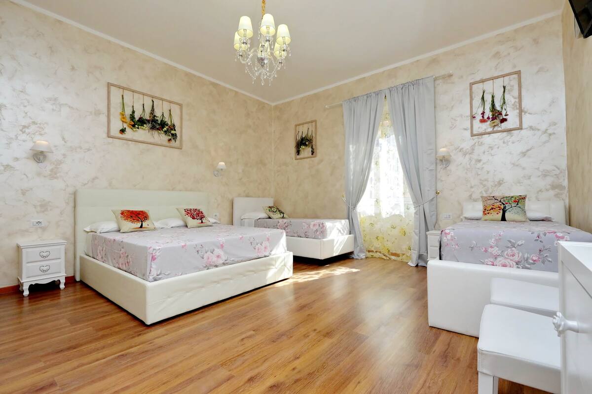 A bedroom with two beds, a nightstand, a desk, and a chandelier.