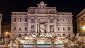 Un edificio imponente con una fuente central y estatuas, rodeado de calles adoquinadas.