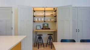 Une cuisine compacte dotée d’un plan de travail en bois, de deux tabourets et d’une étagère intégrée où sont rangés les ustensiles de cuisine.