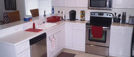 A modern kitchen with white cabinets, stainless steel appliances, a dishwasher, and a red towel hanging on the oven.