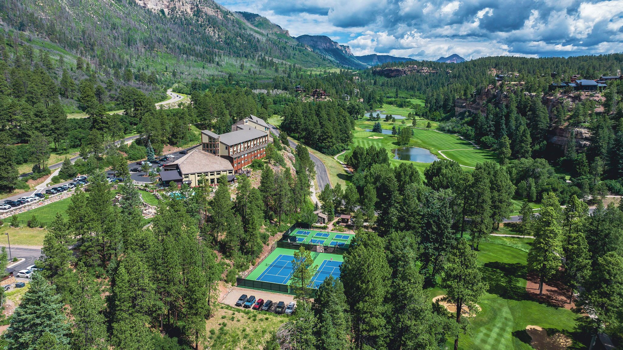 A mountain lodge with a tennis court, a golf course, and a parking area.