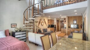A spacious living area with a large dining table, a sofa, and a staircase leading to an upper level. - The Mulligan | AC, Pool, Hot Tub, Golf & Ski (Durango)