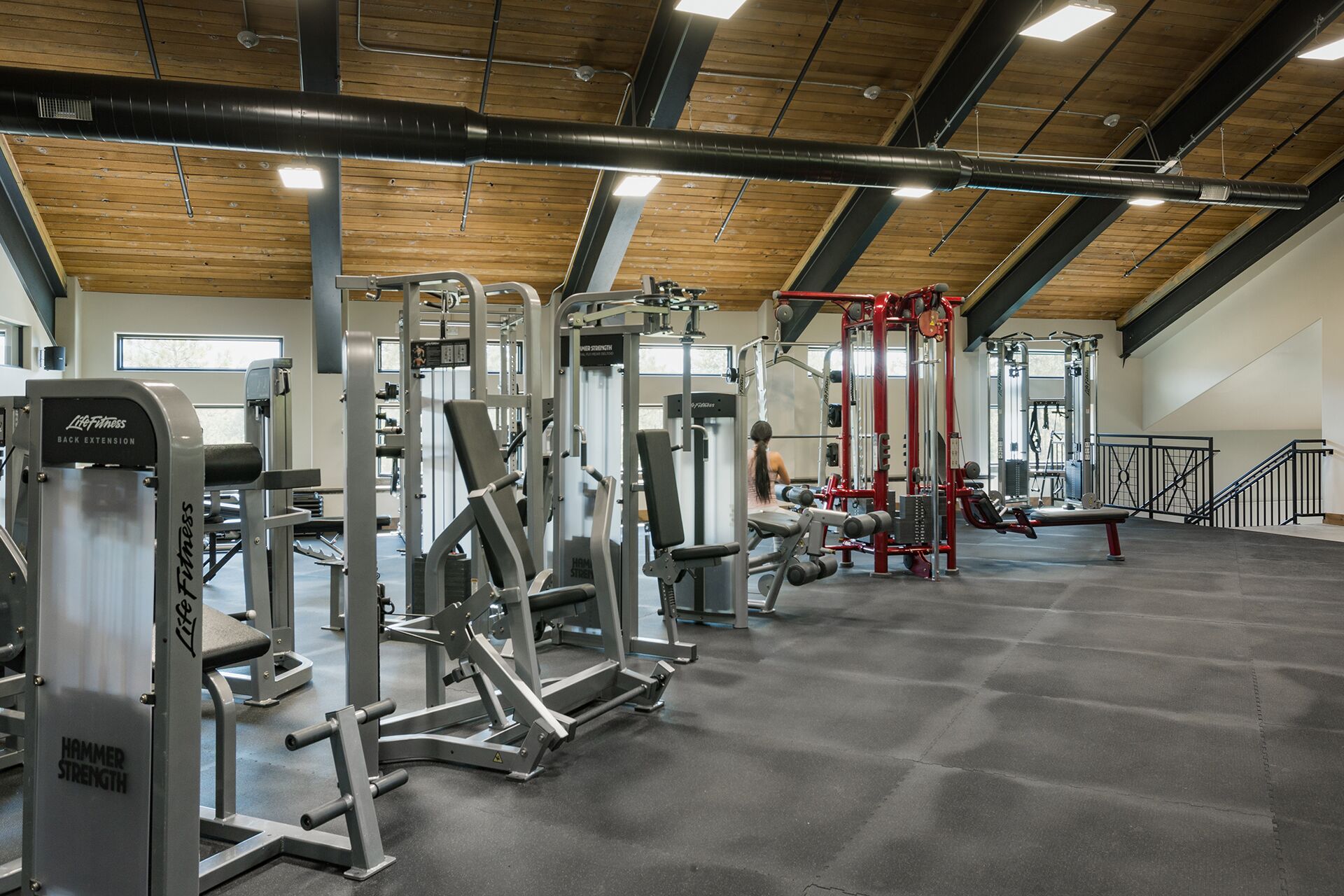 A gym with various exercise machines, a wooden ceiling, and a large window.