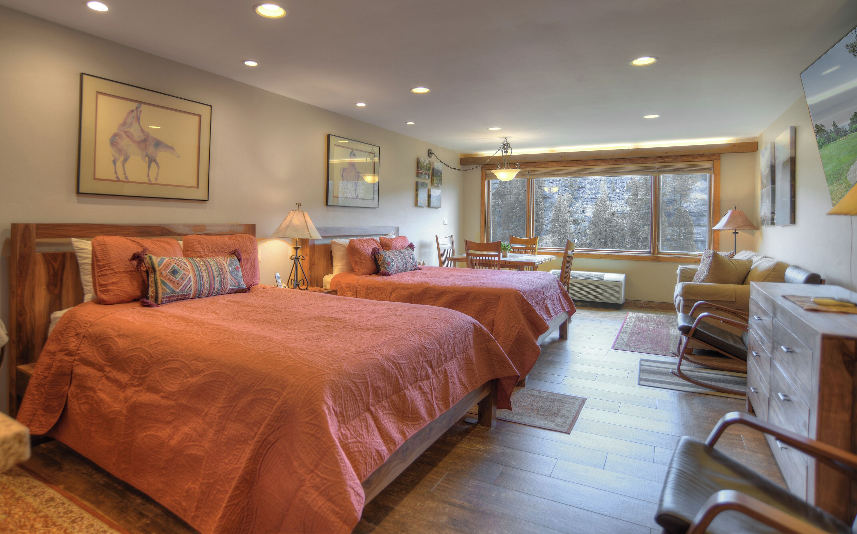 A hotel room with two beds, a desk, a chair, and a large window.