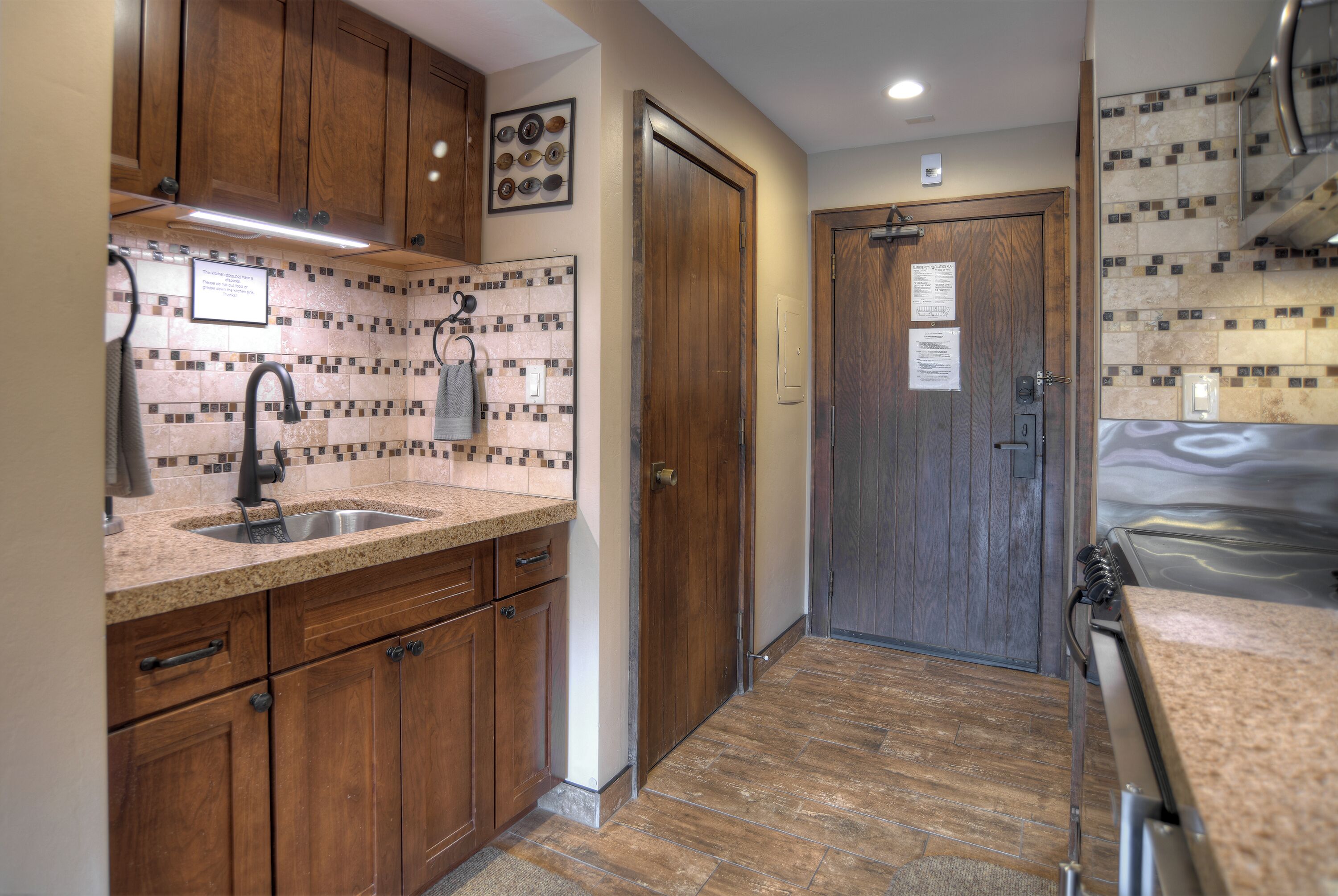 A compact kitchen with wooden cabinets, a granite countertop, and a tiled backsplash.