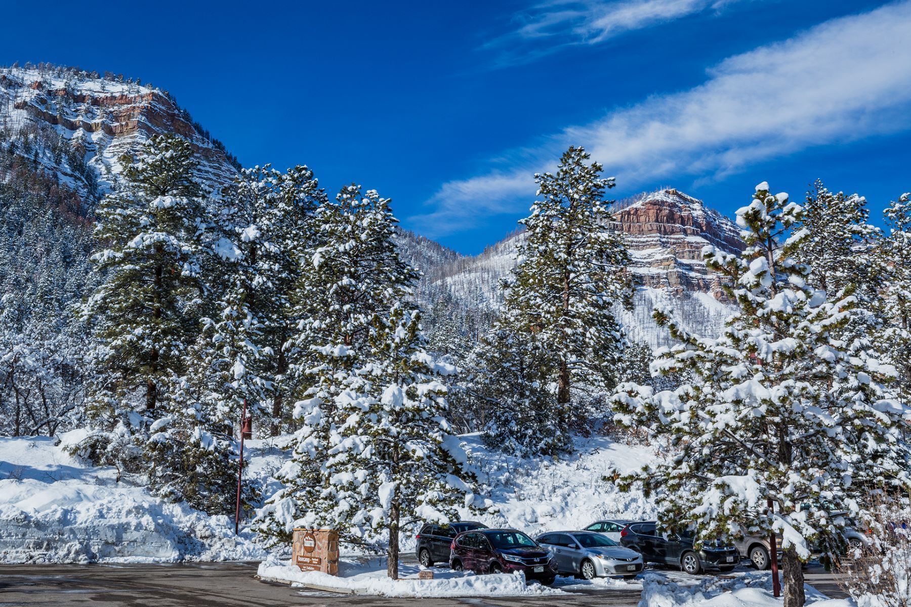 A parking lot with snow-covered trees and a mountain backdrop.