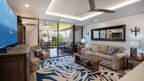 Una sala de estar moderna con un televisor grande, asientos cómodos, un ventilador de techo y vistas al exterior.