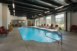 An indoor swimming pool with a metal ladder, surrounded by red chairs and a wooden cabinet with toys.