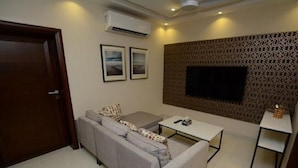 A modern living room with a grey sofa, a coffee table, and a TV mounted on a patterned wall. - Golf Icon Luxury suites  (Lahore)