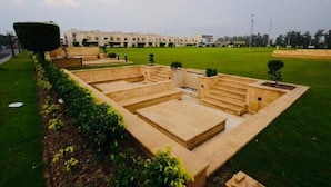 A courtyard with a central open area surrounded by low walls, a building in the background, and a well-maintained lawn. - Golf Icon Luxury suites  (Lahore)