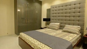A bedroom with a large bed, a wardrobe, and a tufted headboard. - Golf Icon Luxury suites  (Lahore)