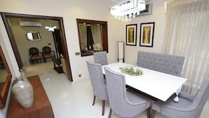 A dining area with a white table, grey upholstered chairs, and a chandelier. - Golf Icon Luxury suites  (Lahore)
