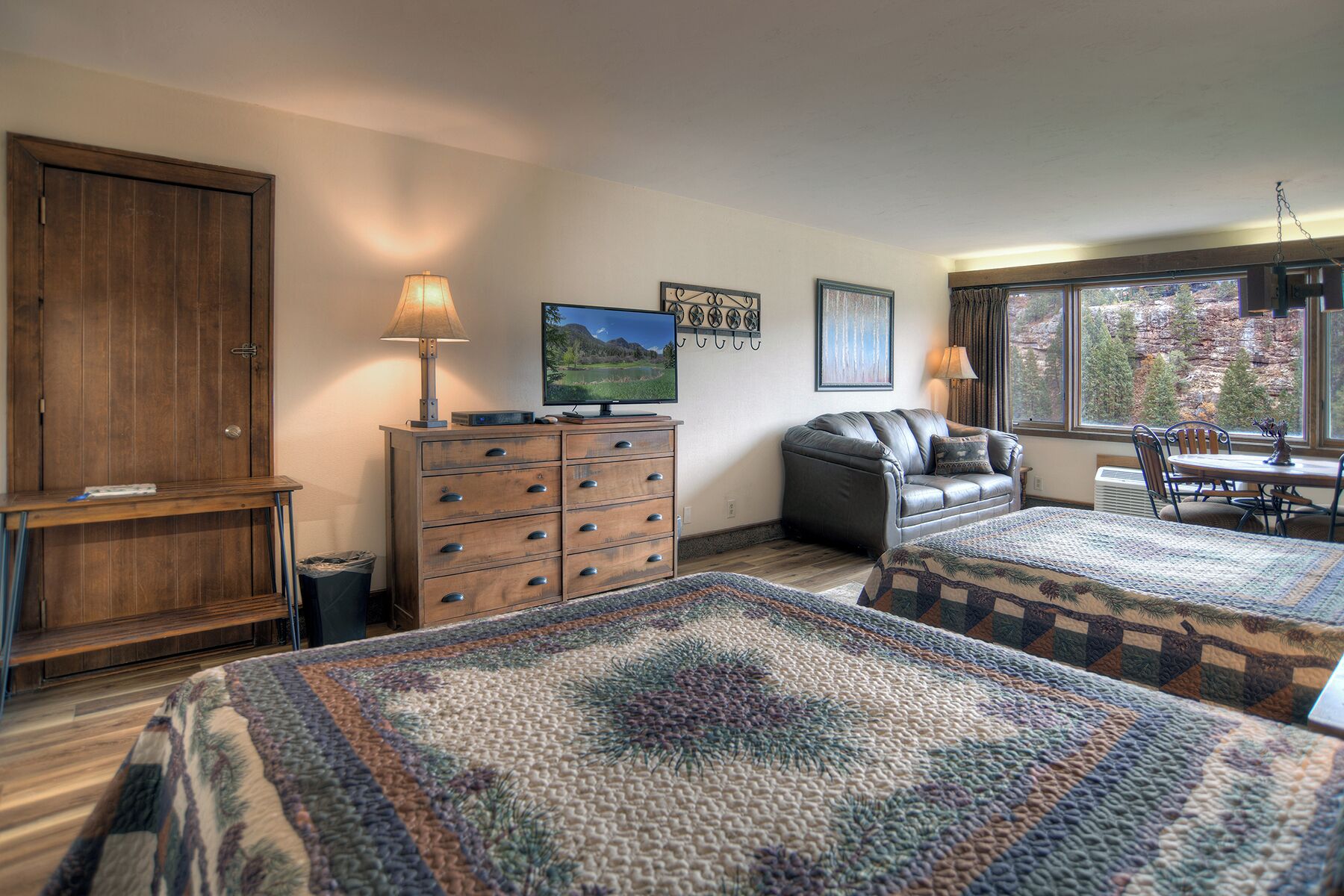 Una habitación acogedora con dos camas, un aparador de madera, un televisor y una ventana con vistas a los árboles.