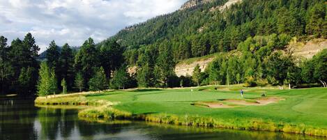 A serene golf course with a lake, surrounded by dense forest and hills.