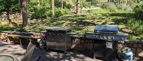An outdoor grill area with a stone wall, a wooden table, and chairs.