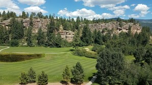 A golf course with a rocky cliff and dense forest in the background.