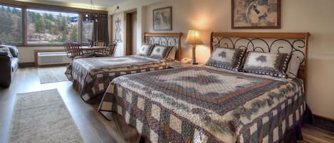 A bedroom with two beds, a dining area, and a view of trees through the window.