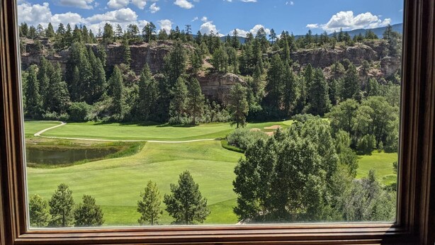 A view of a golf course with a rocky cliff and dense trees in the background.