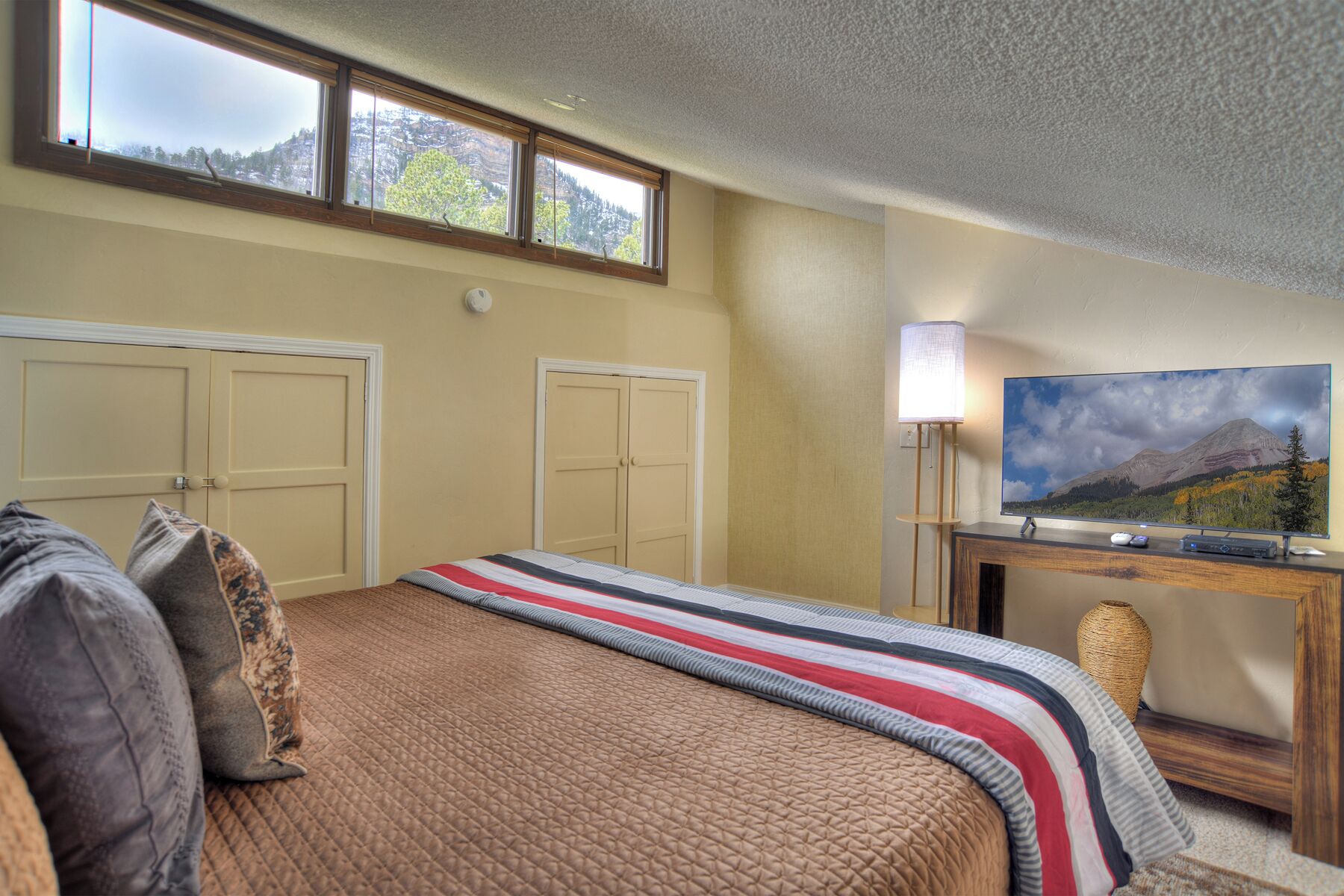 Ein Hotelzimmer mit Bett, zwei Türen, einem Schreibtisch mit Fernseher und Blick auf die Berge.