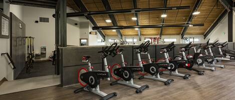Een sportschool met meerdere hometrainers, houten vloeren en een hoge plafond met zichtbare balken.