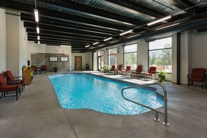 Una piscina interna con una scala in metallo, circondata da sedie rosse e un mobile in legno con giochi.