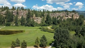 A golf course with a rocky cliff and dense forest in the background.