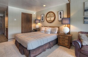 A bedroom with a large bed, bedside tables, a wooden wardrobe, and a leather armchair.