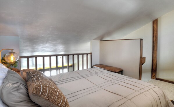 A bedroom with a large bed, a nightstand, a wooden bench, and a view of the outdoors. - Skyline Loft | AC, Pool, Hot Tub, Golf & Ski (Durango)