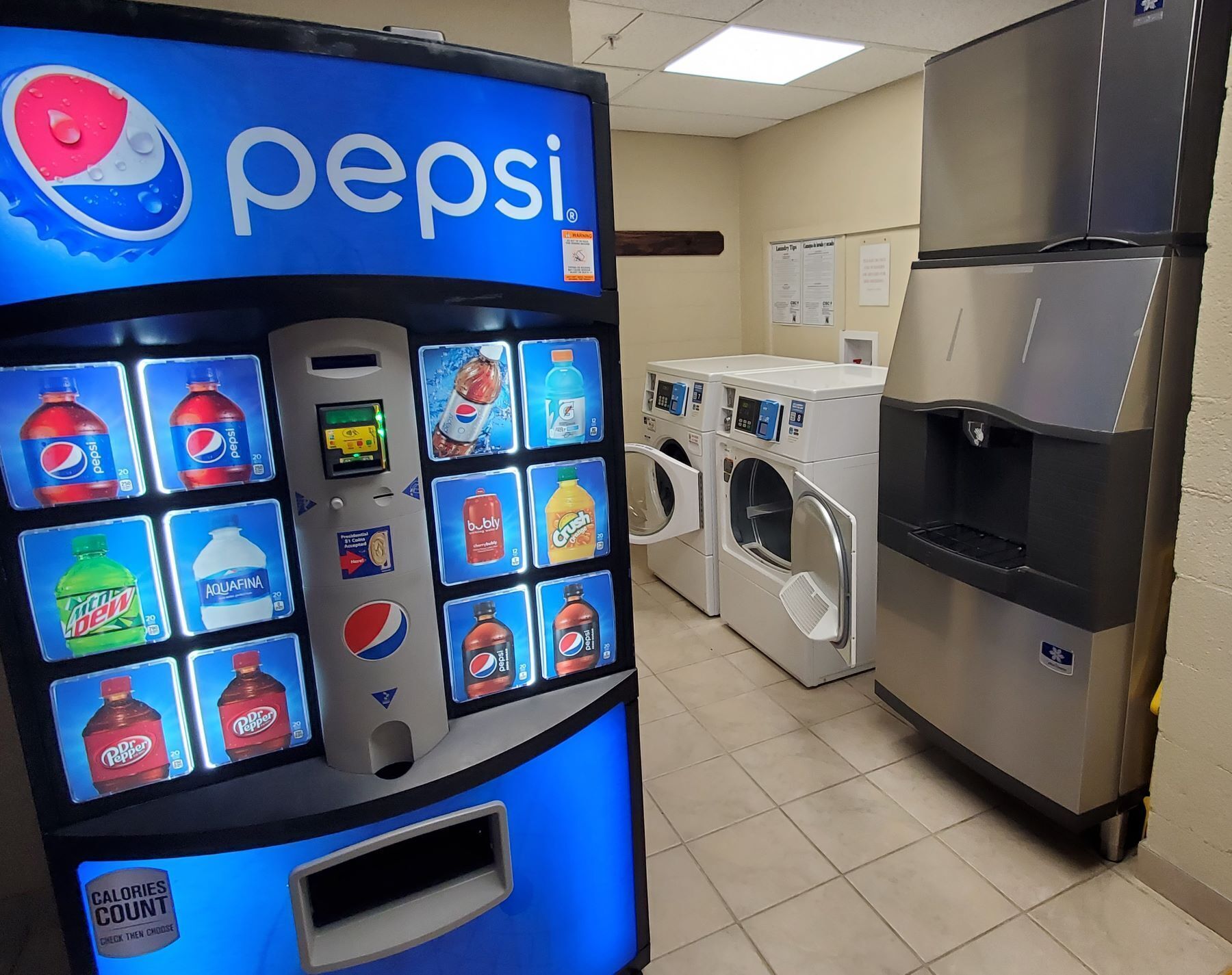 Een automaat met Pepsi en andere dranken, een koelkast en een wasmachine in een kamer.