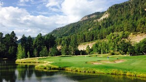 Ein friedlicher Golfplatz mit einem See, umgeben von dichtem Wald und Hügeln.