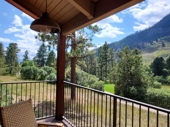 A balcony with a view of a mountainous landscape, a hanging light fixture, and a woven chair.