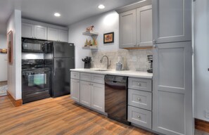 A modern kitchen with stainless steel appliances, grey cabinetry, and a wooden floor.