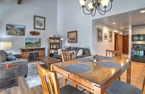 A living room with a fireplace, a dining area with a wooden table and chairs, a kitchen with modern appliances, and a hallway leading to another room.