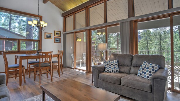 A spacious living room with a large window, a dining area with wooden furniture, and a grey sofa with patterned cushions. - Whistle Stop | AC, Pool, Hot Tub, Golf & Ski (Durango)