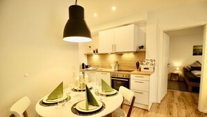 Una cocina compacta con armarios blancos, una estufa y un comedor con una mesa redonda preparada para cuatro personas.