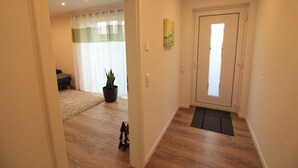 Un pasillo con suelo de madera, una puerta con ventanal, una planta en maceta y un pequeño tapete.