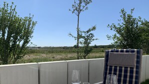 Mesa para dos con mantel a cuadros, platos blancos y copas de vino, con vistas a un campo de césped y árboles.